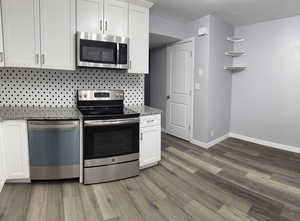 Kitchen featuring white cabinetry, light stone counters, a textured ceiling, stainless steel appliances, and hardwood / wood-style floors