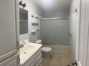 Full bathroom with tile patterned flooring, vanity, shower / bath combination with glass door, and toilet