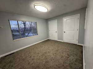 Unfurnished bedroom featuring a textured ceiling and dark carpet