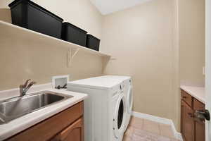 Laundery room features a utility  sink, shelf, cabinets, washer and dryer