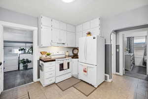 Kitchen featuring light tile patterned floors, white appliances, backsplash, white cabinets, and washer / dryer