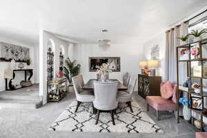 Carpeted dining space featuring a notable chandelier and a textured ceiling