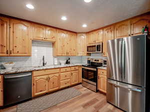 Kitchen featuring tasteful backsplash, sink, stainless steel appliances, granite countertops with custom cabinets, and lvp flooring