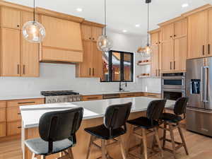 Kitchen with light hardwood / wood-style flooring, hanging light fixtures, stainless steel appliances, a center island, and light brown cabinetry