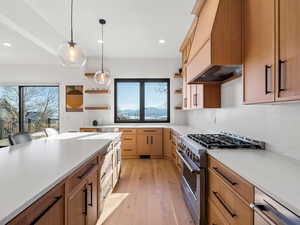 Kitchen with pendant lighting, high end range, tasteful backsplash, light stone countertops, and light hardwood / wood-style floors