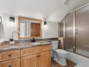 Full bathroom featuring shower / bath combination with glass door, tile walls, vanity, tile patterned floors, and toilet