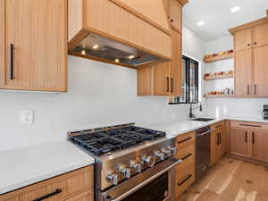 Kitchen with premium range hood, sink, stainless steel appliances, light brown cabinets, and light hardwood / wood-style flooring