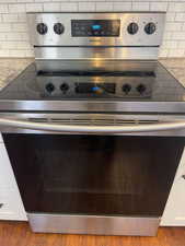 Details featuring white cabinetry, tasteful backsplash, wood-type flooring, and stainless steel electric range