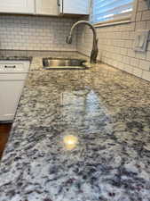 Kitchen featuring white cabinetry, sink, decorative backsplash, and dark stone counters