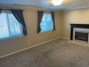 Unfurnished living room with ornamental molding, carpet flooring, a tile fireplace, and a textured ceiling