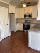 Kitchen with dark wood-type flooring, vaulted ceiling, white cabinets, and appliances with stainless steel finishes