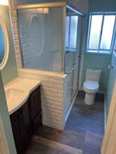 Bathroom with hardwood / wood-style flooring, vanity, toilet, and a shower with shower door