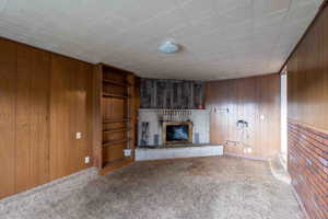 Unfurnished family room with carpet floors, a fireplace, built in features, and paneled walls