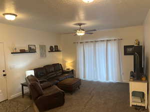 Carpeted living room featuring ceiling fan and a textured ceiling