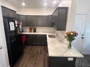 Kitchen featuring black fridge, dark wood-style flooring, sink, and light stone counters