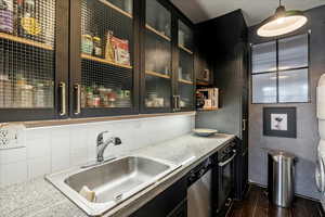 Kitchen featuring sink, decorative light fixtures, dishwasher, black oven, and stacked washer / dryer