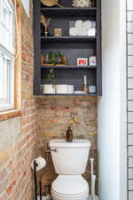 Bathroom with a wealth of natural light, toilet, and brick wall