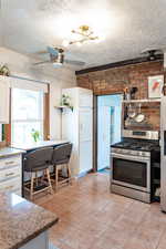 Kitchen with light tile patterned flooring, white cabinetry, a textured ceiling, appliances with stainless steel finishes, and brick wall