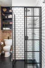 Bathroom with toilet, a shower with door, and tile patterned flooring