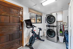 Exercise room with stacked washer and clothes dryer and light hardwood / wood-style flooring