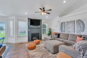 Living room featuring vaulted ceiling, ceiling fan, a fireplace, and light wood-type flooring