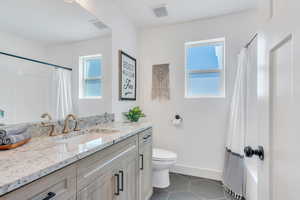 Bathroom with tile patterned flooring, vanity, toilet, and a healthy amount of sunlight