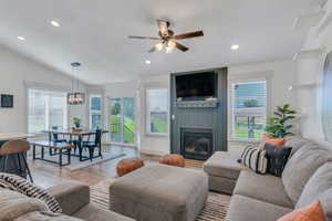 Living room with lofted ceiling, ceiling fan with notable chandelier, a fireplace, and light hardwood / wood-style flooring