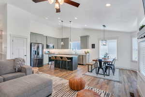 Living room with ceiling fan, high vaulted ceiling, light hardwood / wood-style floors, and sink