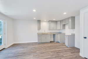 Kitchen featuring light stone counters, gray cabinets, sink, and light wood-type flooring