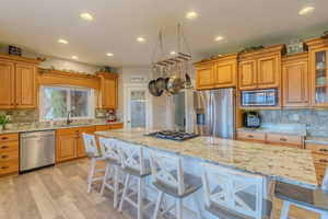 Kitchen featuring sink, a breakfast bar area, stainless steel appliances, a center island, and light stone counters