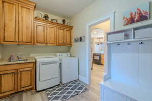 Clothes washing area with washer and dryer, sink, light hardwood / wood-style flooring, and cabinets