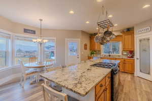 Kitchen featuring sink, black gas stove, light hardwood / wood-style floors, a kitchen island, and decorative light fixtures