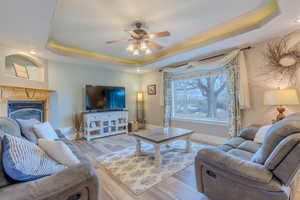 Living room with ceiling fan, a tray ceiling, and light hardwood / wood-style floors