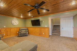 Carpeted living room featuring wood ceiling, ceiling fan, ornamental molding, and wood walls