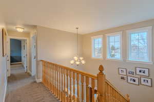 Hallway featuring light carpet and a notable chandelier