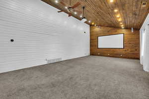 Cinema room featuring carpet flooring, wooden ceiling, ceiling fan, and wood walls