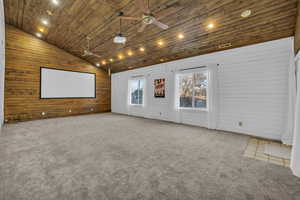 Home theater room featuring lofted ceiling, wood walls, wood ceiling, carpet flooring, and ceiling fan