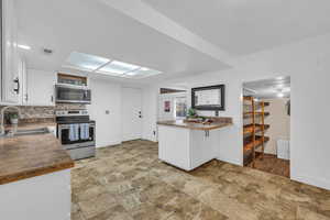 Kitchen featuring white cabinetry, sink, decorative backsplash, kitchen peninsula, and stainless steel appliances