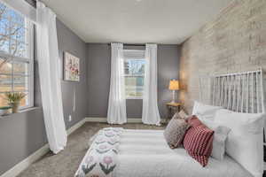 Bedroom featuring multiple windows, light carpet, a textured ceiling, and brick wall