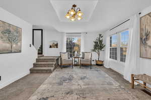 Living area with plenty of natural light, carpet floors, a chandelier, and a tray ceiling