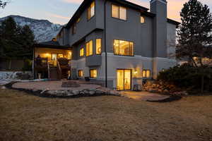 Back house at dusk featuring a patio area and a lawn