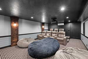 Home theater featuring light colored carpet, a wall mounted AC, and a textured ceiling