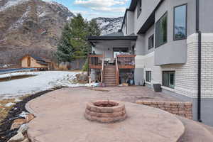 Snow covered patio with a deck with mountain view, a trampoline, and an outdoor fire pit