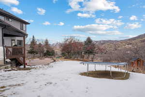 Yard covered in snow with a mountain view and a trampoline