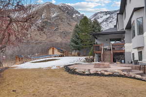 Yard layered in snow featuring a shed, a mountain view, a patio area, and a trampoline