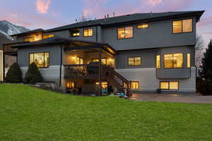 Back of house at dusk with brick siding, a patio area, stairs, a yard, and stucco siding