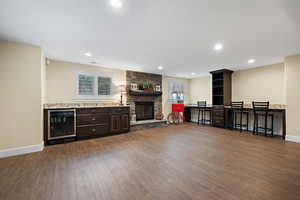 Living room featuring beverage cooler, dark hardwood / wood-style flooring, and a stone fireplace