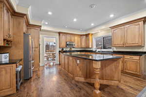 Kitchen with dark hardwood / wood-style flooring, a kitchen island, dark stone counters, and appliances with stainless steel finishes