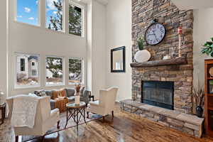 Living room featuring hardwood / wood-style flooring, plenty of natural light, a stone fireplace, and a high ceiling