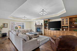 Living room featuring a tray ceiling, dark wood-type flooring, a chandelier, and a textured ceiling